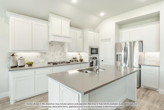 kitchen featuring lofted ceiling, sink, appliances with stainless steel finishes, white cabinetry, and a center island with sink