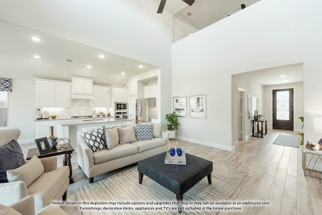 living room featuring ceiling fan, high vaulted ceiling, sink, and light hardwood / wood-style floors