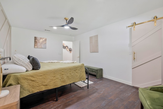 bedroom with a barn door, dark wood-type flooring, and ceiling fan