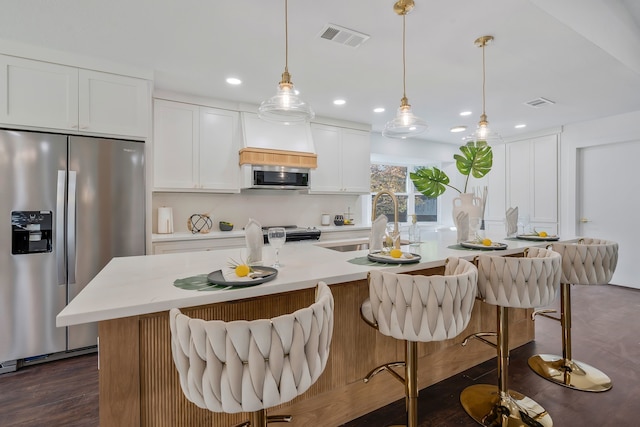 kitchen featuring pendant lighting, stainless steel appliances, an island with sink, and white cabinets