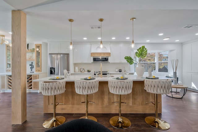 kitchen featuring a kitchen bar, white cabinetry, decorative light fixtures, stainless steel appliances, and a kitchen island with sink