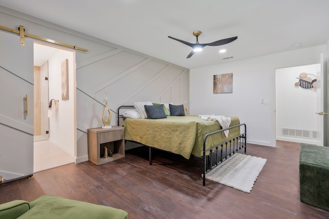 bedroom with dark hardwood / wood-style flooring, a barn door, and ceiling fan