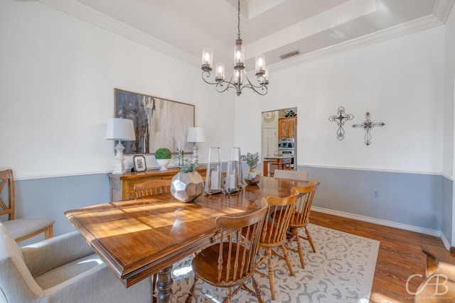 dining space featuring crown molding, a tray ceiling, a chandelier, and hardwood / wood-style floors