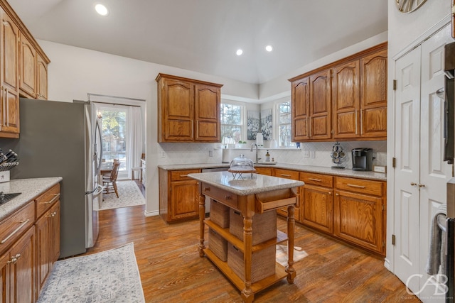 kitchen with wood-type flooring, sink, stainless steel fridge, backsplash, and a center island