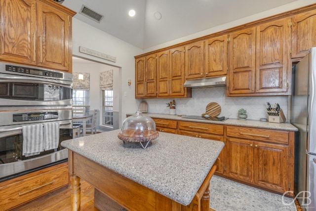 kitchen featuring appliances with stainless steel finishes, lofted ceiling, decorative backsplash, a center island, and light stone countertops