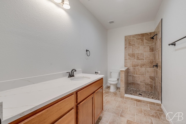 bathroom featuring vanity, a tile shower, and toilet