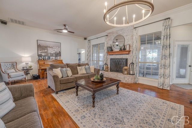 living room with ornamental molding, wood-type flooring, a fireplace, and ceiling fan with notable chandelier