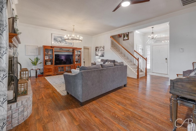 living room with dark wood-type flooring, a fireplace, ornamental molding, and ceiling fan with notable chandelier