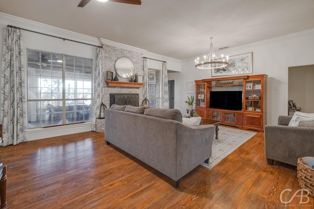 living room featuring ornamental molding, a brick fireplace, dark hardwood / wood-style floors, and ceiling fan with notable chandelier