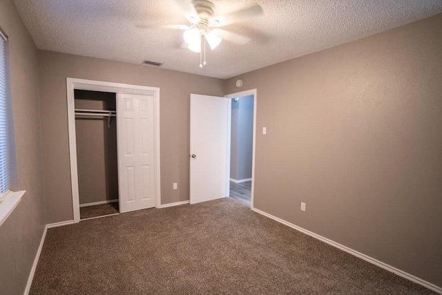 unfurnished bedroom with ceiling fan, a textured ceiling, a closet, and dark colored carpet