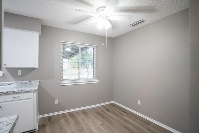 unfurnished dining area with a textured ceiling, ceiling fan, and light wood-type flooring