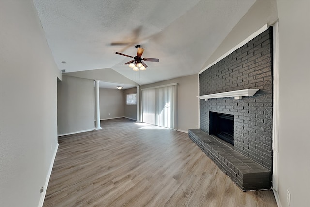 unfurnished living room featuring lofted ceiling, a brick fireplace, light wood-type flooring, a textured ceiling, and ceiling fan