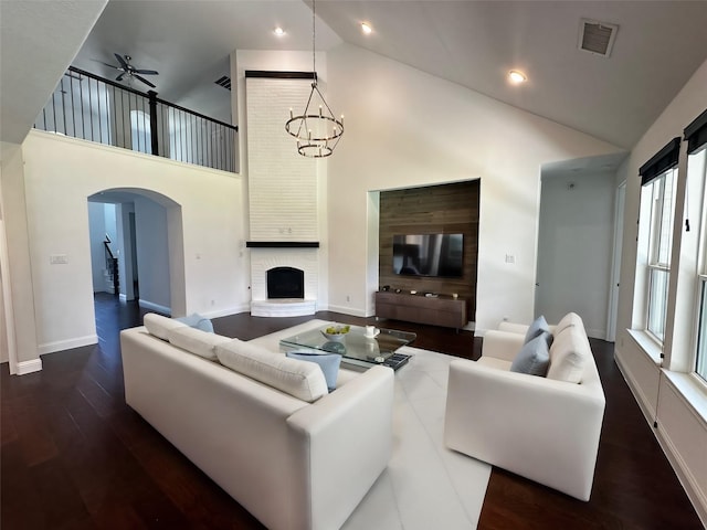 living room featuring a brick fireplace, dark wood-type flooring, ceiling fan with notable chandelier, and high vaulted ceiling