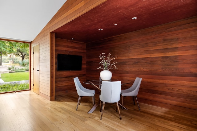 unfurnished dining area featuring light hardwood / wood-style flooring, vaulted ceiling, and wooden walls