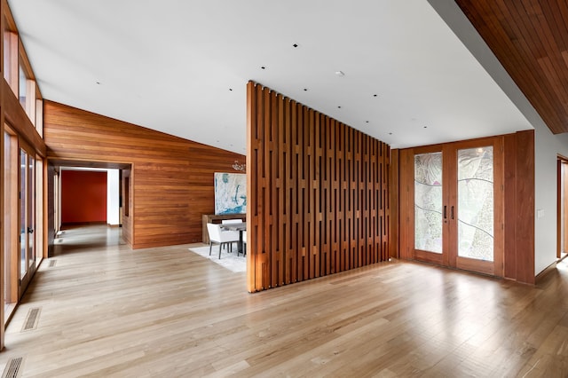 unfurnished living room featuring lofted ceiling, wooden walls, light hardwood / wood-style floors, and french doors