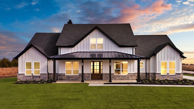 back house at dusk with covered porch and a lawn