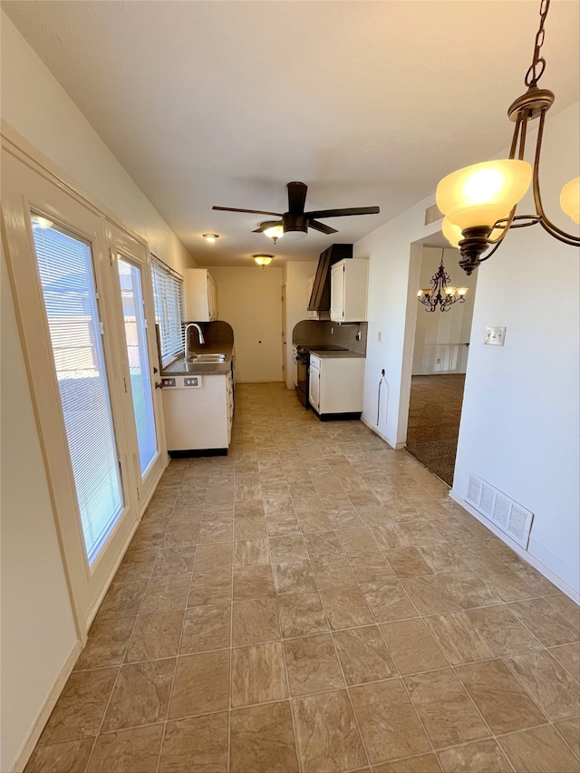 interior space featuring ceiling fan with notable chandelier, pendant lighting, white cabinetry, sink, and wall chimney range hood