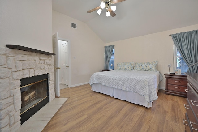 bedroom featuring a fireplace, light hardwood / wood-style floors, ceiling fan, and vaulted ceiling