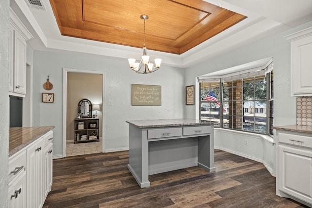 kitchen featuring a tray ceiling, decorative light fixtures, light stone countertops, and white cabinets