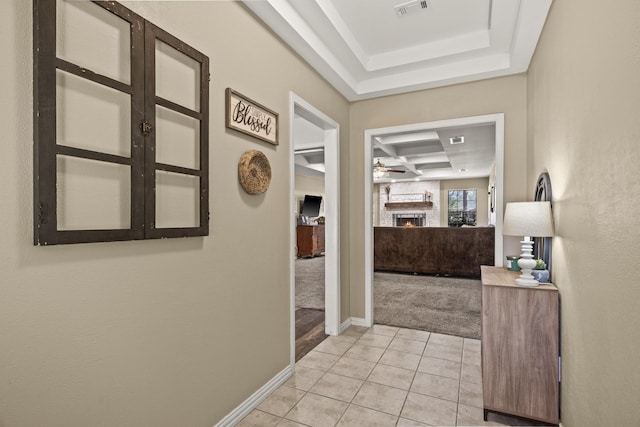 hallway with coffered ceiling, a raised ceiling, and light tile patterned floors