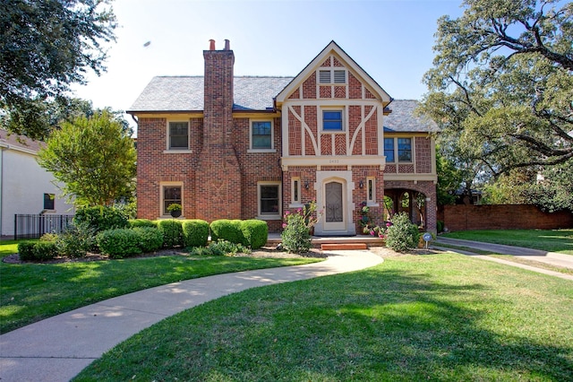 english style home with brick siding, a front lawn, and fence