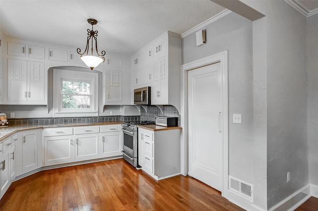 kitchen featuring wood finished floors, visible vents, white cabinetry, appliances with stainless steel finishes, and crown molding