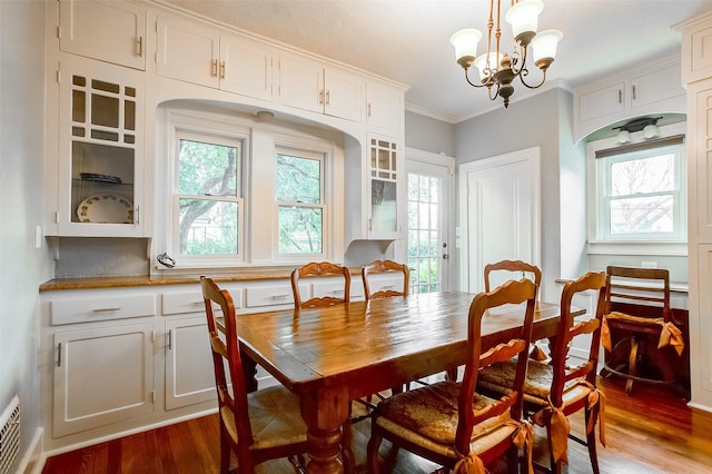 dining space with a notable chandelier, plenty of natural light, ornamental molding, and dark wood-style flooring