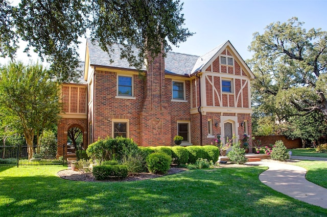 english style home featuring brick siding, fence, and a front lawn