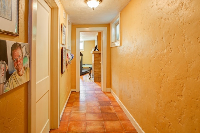 hallway with light tile patterned flooring, baseboards, a textured ceiling, and a textured wall