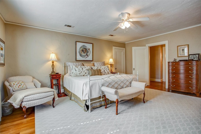 bedroom with ceiling fan, visible vents, wood finished floors, and ornamental molding