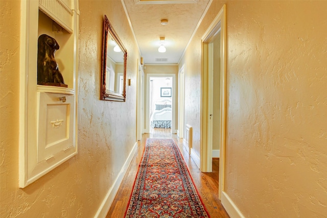 corridor featuring baseboards, visible vents, wood finished floors, and a textured wall