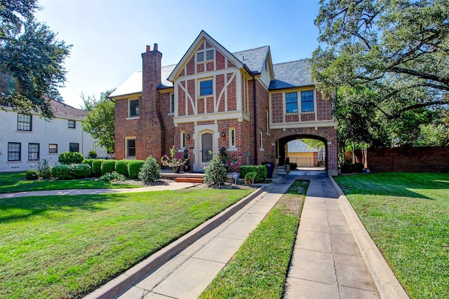 tudor-style house with a chimney, a front lawn, and brick siding