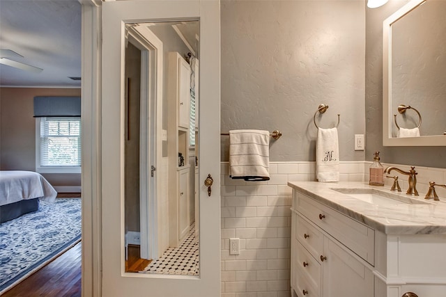 ensuite bathroom featuring a textured wall, a wainscoted wall, wood finished floors, vanity, and tile walls