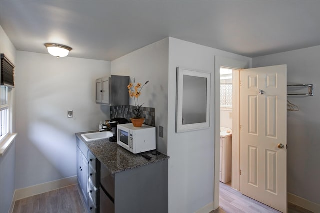 kitchen featuring white microwave, a sink, baseboards, light wood-style floors, and dark stone counters