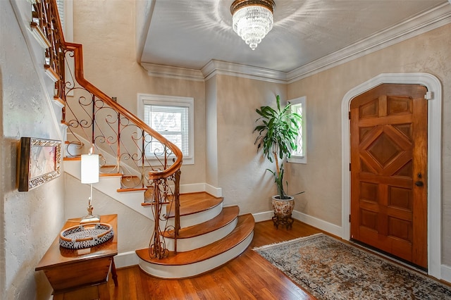 foyer entrance featuring arched walkways, a chandelier, wood finished floors, baseboards, and ornamental molding