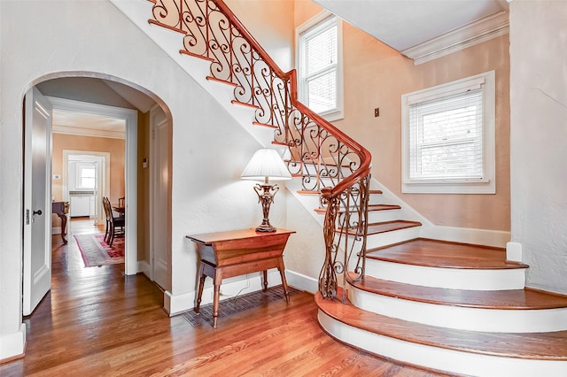 staircase featuring arched walkways, crown molding, baseboards, and wood finished floors