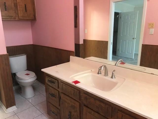 bathroom with tile patterned flooring, vanity, wooden walls, and toilet