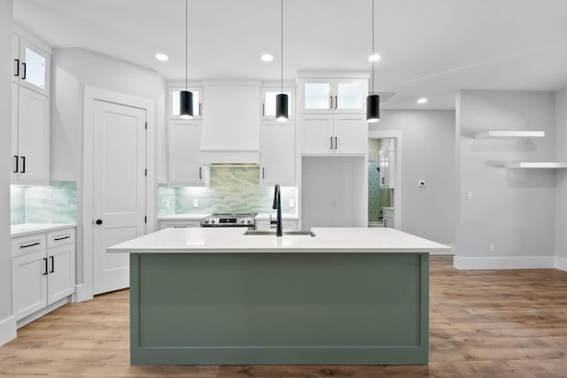 kitchen featuring a kitchen island with sink, sink, pendant lighting, and white cabinets