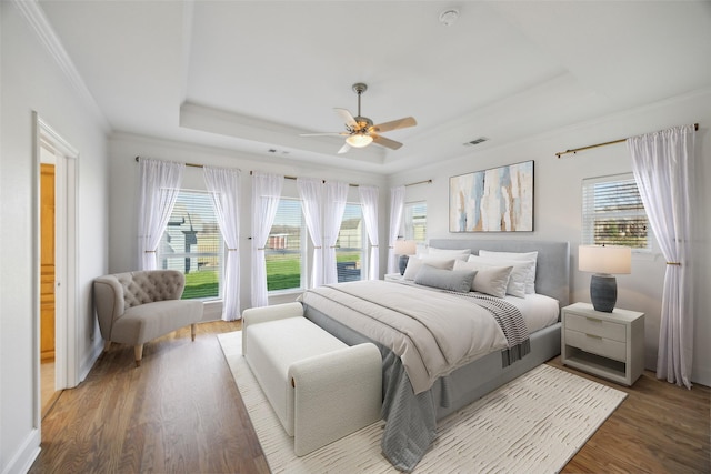 bedroom featuring a raised ceiling, ornamental molding, hardwood / wood-style flooring, and ceiling fan