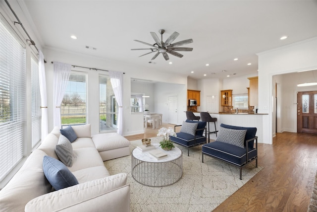 living room with ornamental molding, sink, ceiling fan, and light hardwood / wood-style flooring