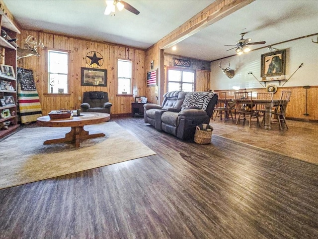 living room with dark wood-type flooring, ceiling fan, and wood walls