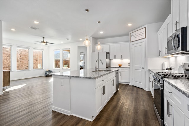 kitchen featuring decorative light fixtures, white cabinetry, sink, stainless steel appliances, and a center island with sink