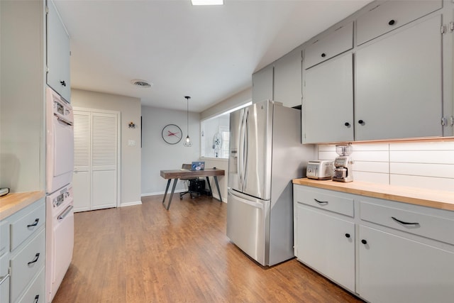 kitchen with pendant lighting, tasteful backsplash, white cabinetry, oven, and stainless steel fridge with ice dispenser