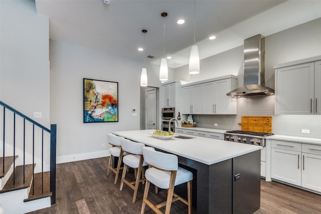 kitchen featuring decorative light fixtures, tasteful backsplash, sink, a kitchen island with sink, and wall chimney range hood