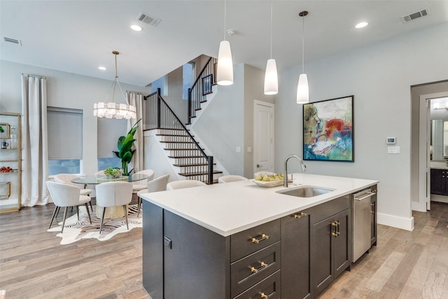 kitchen with pendant lighting, sink, a kitchen island with sink, light hardwood / wood-style floors, and stainless steel dishwasher