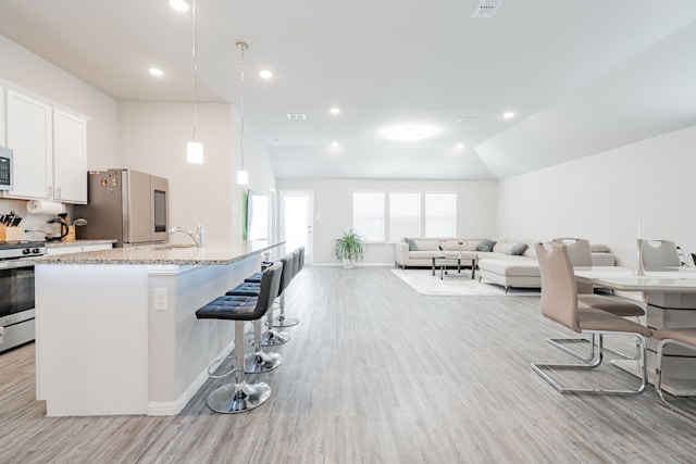 kitchen featuring a breakfast bar area, stainless steel appliances, light stone countertops, white cabinets, and vaulted ceiling