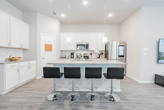 kitchen with appliances with stainless steel finishes, white cabinetry, backsplash, hanging light fixtures, and light stone counters