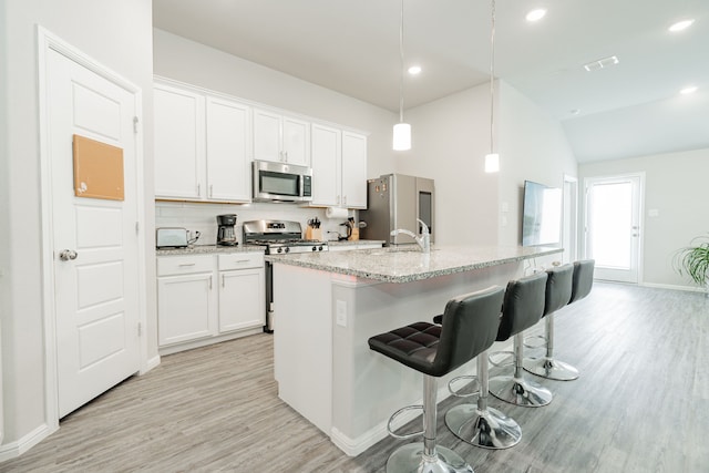 kitchen with hanging light fixtures, white cabinetry, appliances with stainless steel finishes, and a kitchen island with sink