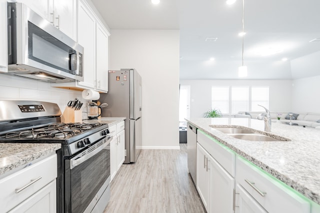 kitchen with sink, hanging light fixtures, stainless steel appliances, light stone countertops, and white cabinets