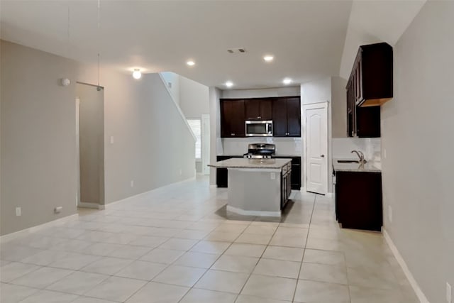 kitchen featuring sink, light tile patterned floors, appliances with stainless steel finishes, dark brown cabinetry, and a kitchen island